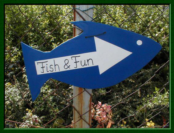 Ein blauer Holzfisch mit Pfeil und der Aufschrift "Fisch & Fun" hngt an einem Zaun